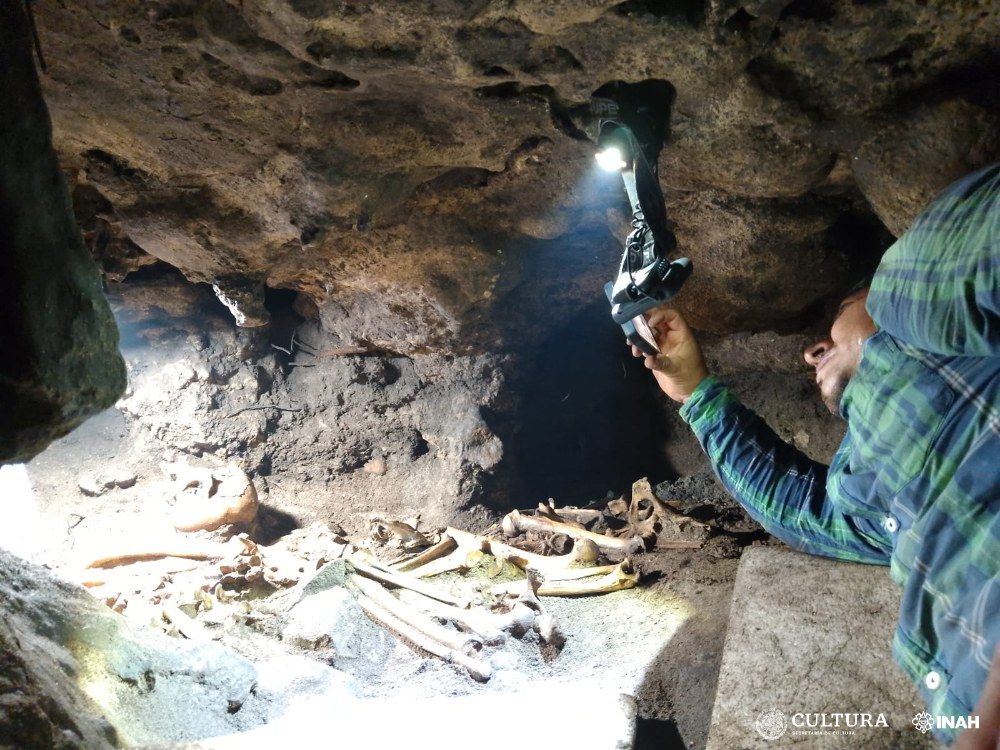 One of the excavation team takes a photo of some bones inside the cave, holding a bright light.